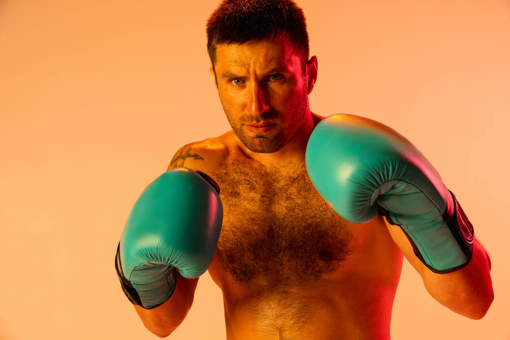 Close-up professionele mannelijke bokser in sportkleding en handschoenen geïsoleerd op gele studio achtergrond in neon licht. Begrip sport, activiteit, beweging, welzijn. - Foto, afbeelding