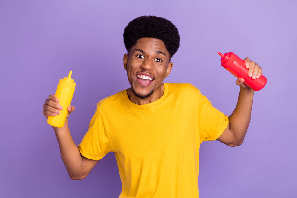 Portret atrakcyjnego beztroskiego wesołego faceta trzymającego butelki ketchupu bawiącego się wyizolowanym na fioletowym fioletowym tle - Zdjęcie, obraz