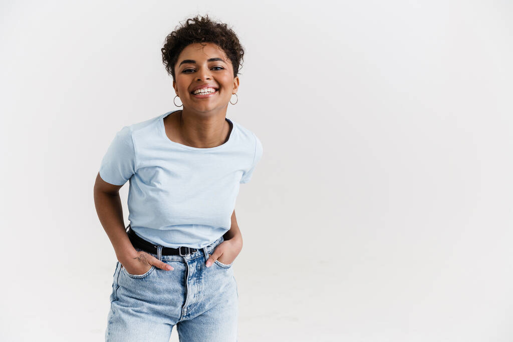 junge schwarze Frau im T-Shirt lächelt und blickt isoliert in die Kamera vor weißem Hintergrund - Foto, Bild