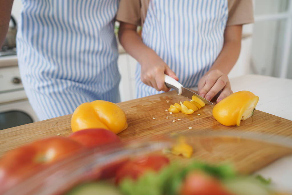 Nahaufnahme einer Frau und eines Mädchens, die in der Küche Gemüse für Salate schneiden - Foto, Bild