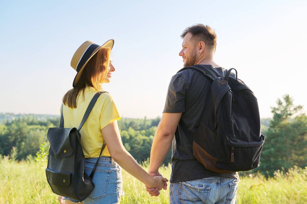 Счастливая взрослая пара с рюкзаками, держащиеся за руки, вид сзади - Фото, изображение