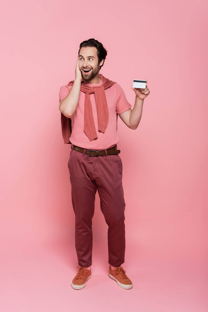 Ενθουσιασμένος άνθρωπος κρατώντας πιστωτική κάρτα σε ροζ φόντο  - Φωτογραφία, εικόνα