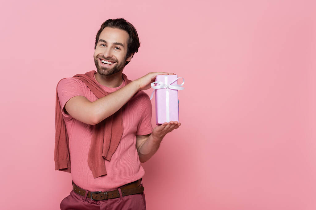 Улыбающийся мужчина держит подарочную коробку с лентой, изолированной на розовый  - Фото, изображение