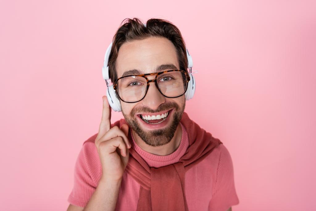 Uomo sorridente in occhiali e cuffie guardando la fotocamera isolata su rosa  - Foto, immagini