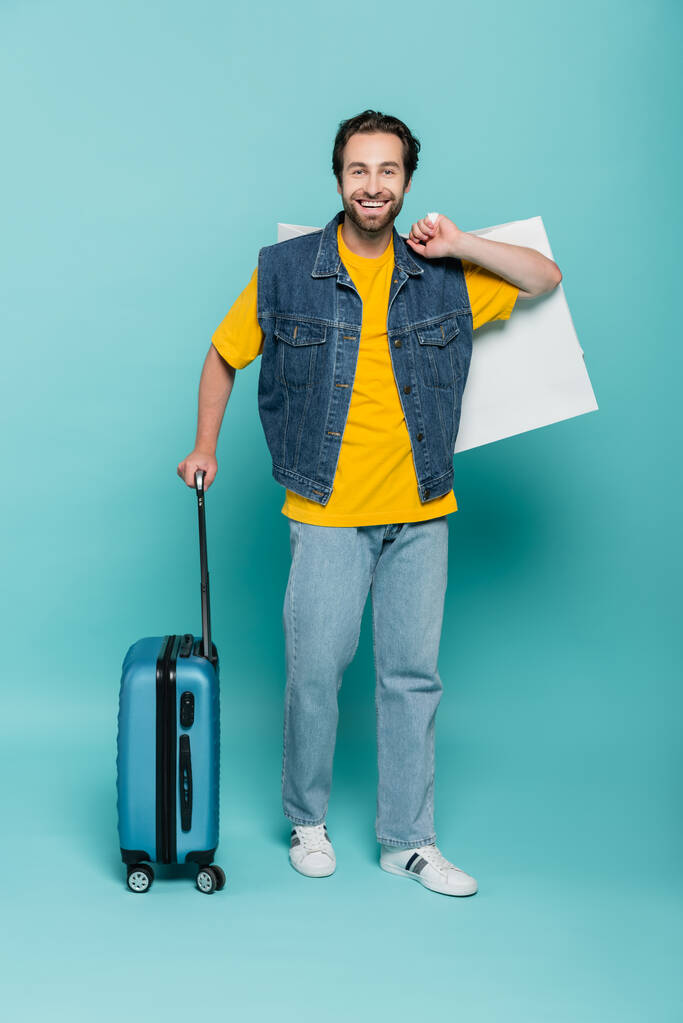 Positieve man met boodschappentas en koffer op blauwe achtergrond  - Foto, afbeelding