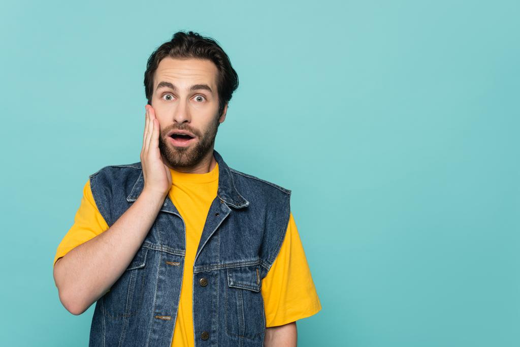 Shocked man in denim vest looking at camera isolated on blue  - Photo, Image
