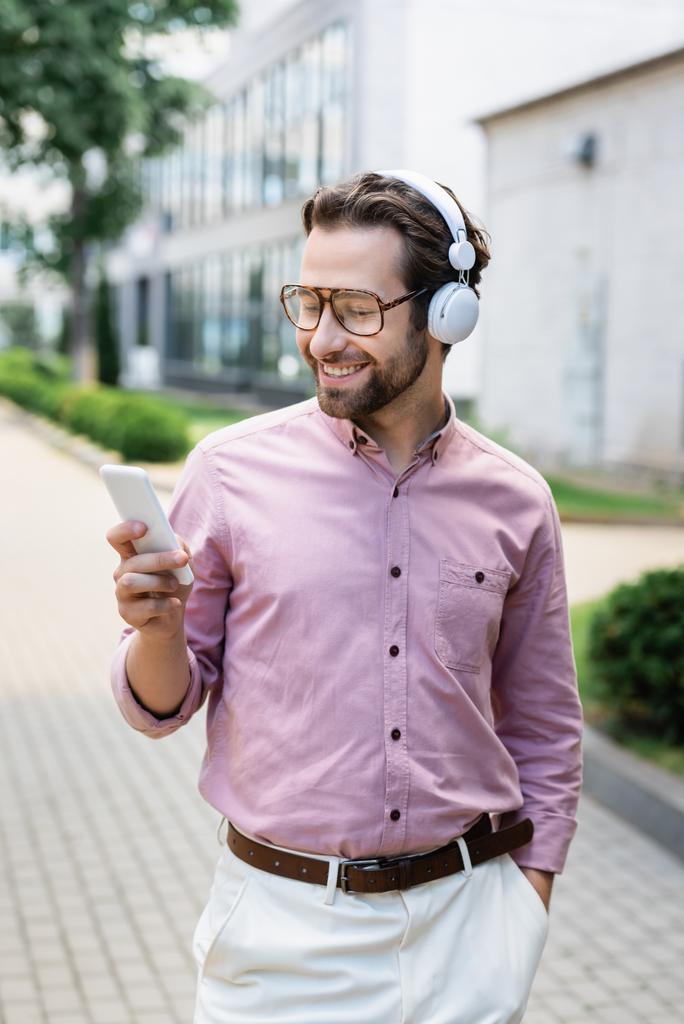 Θετικός επιχειρηματίας σε ακουστικά χρησιμοποιώντας smartphone σε αστικό δρόμο  - Φωτογραφία, εικόνα