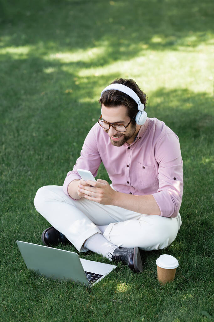Fiatal üzletember a fülhallgatóban, a kávéhoz közeli eszközöket használ, hogy a parkba menjen.  - Fotó, kép