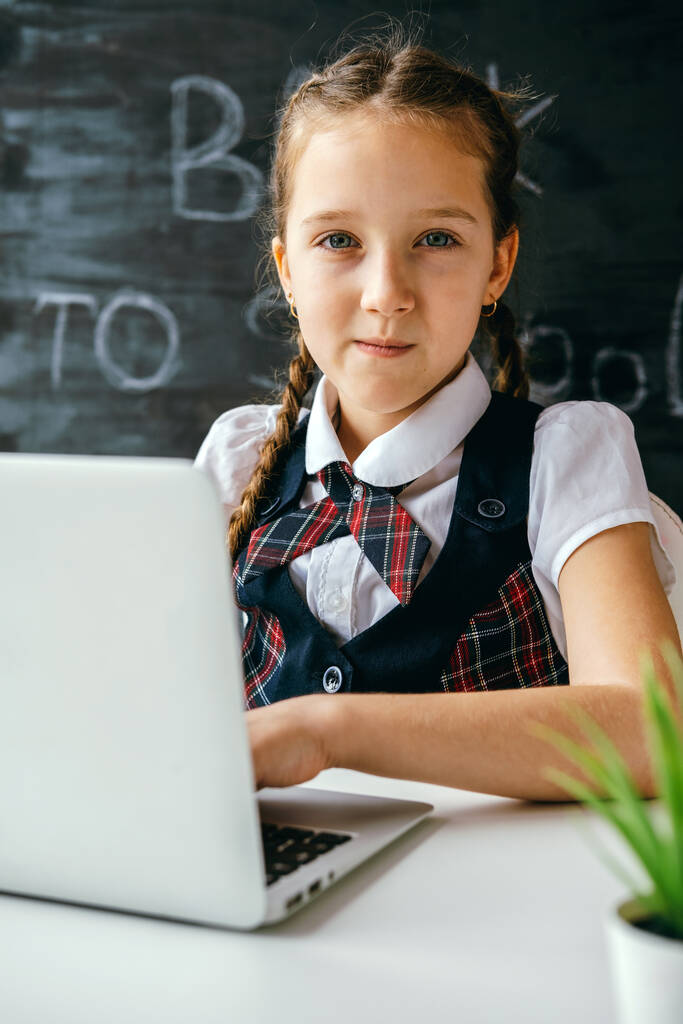 Χαριτωμένο κοριτσάκι που κάθεται στο γραφείο και χρησιμοποιεί υπολογιστή. Επιστροφή στο σχολείο και online μαθήματα έννοια. - Φωτογραφία, εικόνα
