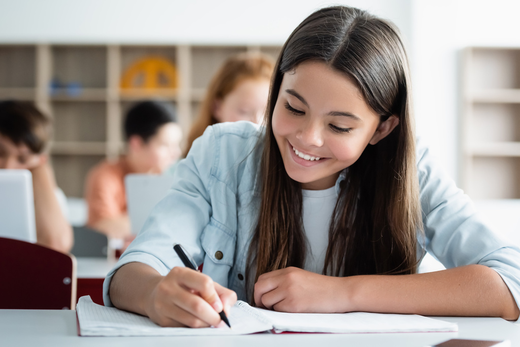 Estudante sorrindo escrevendo no caderno em sala de aula  - Foto, Imagem