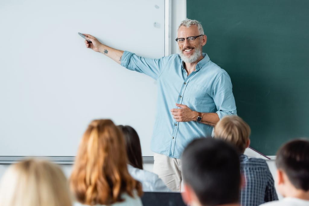 Uśmiechnięty nauczyciel wskazujący na tablicę z wymazanymi źrenicami  - Zdjęcie, obraz