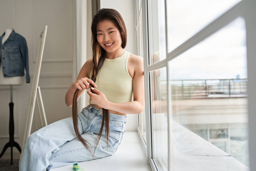 Woman looking at the camera with wide smile while combing her hair - Photo, Image