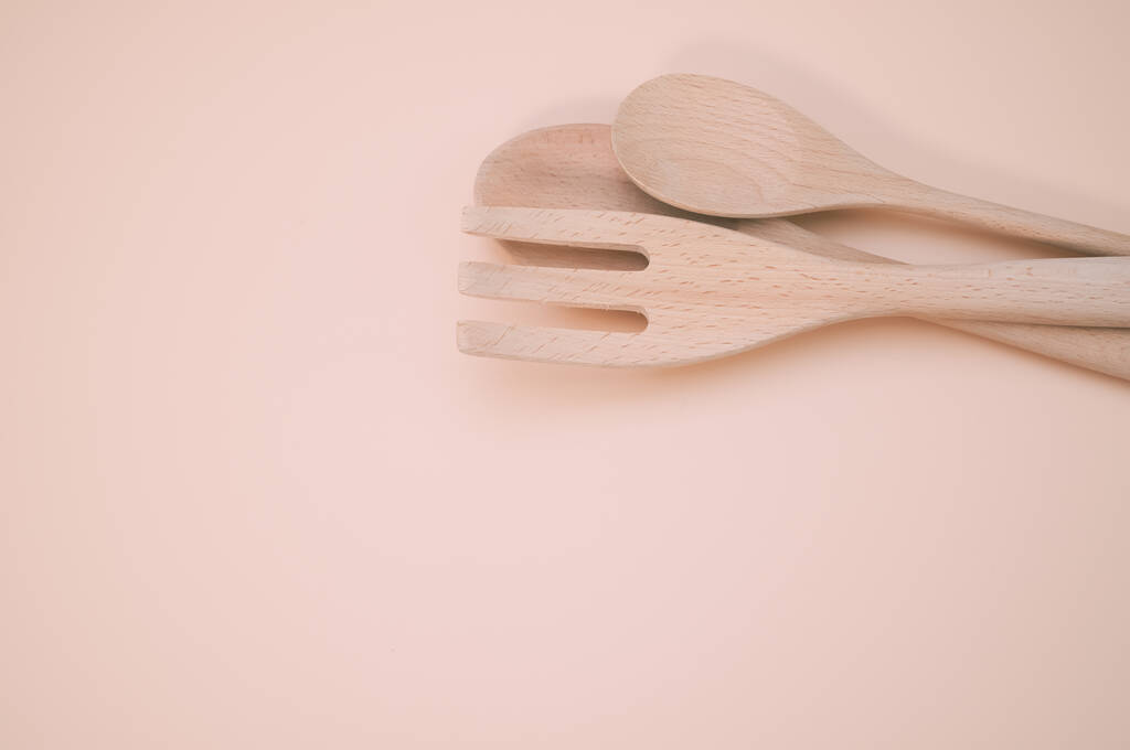 Un primo piano di cucchiai di legno e forchetta isolati su uno sfondo rosa con spazio libero per il testo - Foto, immagini