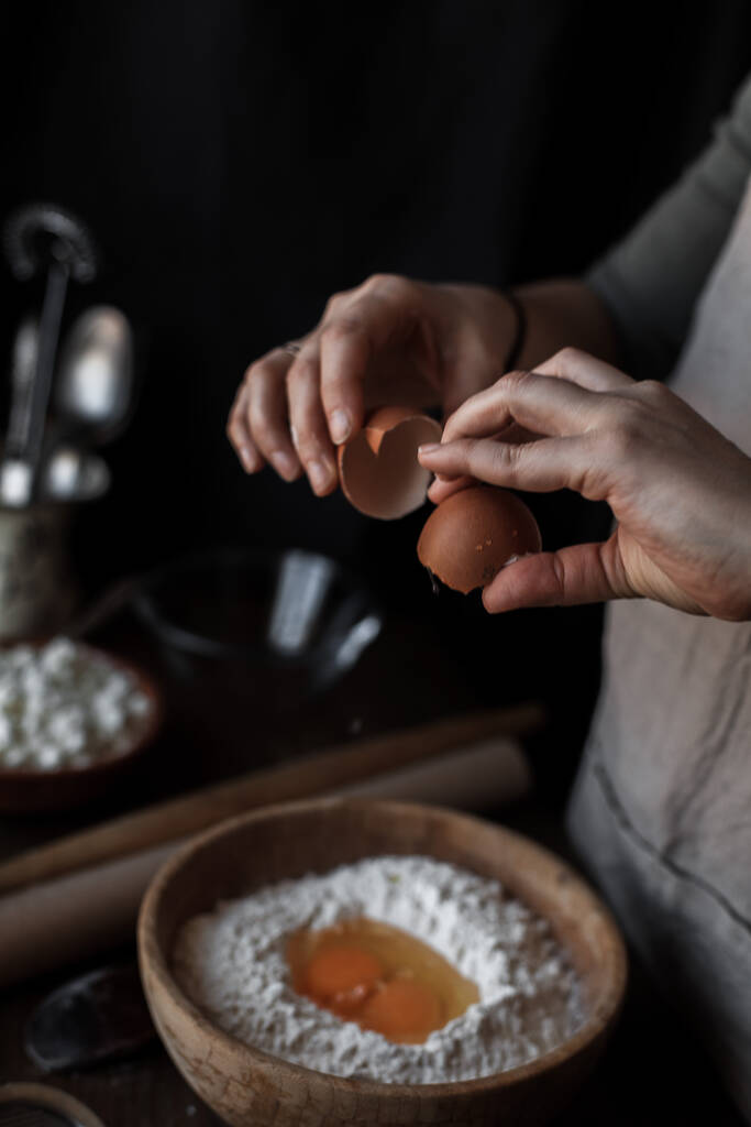 Вертикальний знімок жіночих рук додавання яєць до тіста в дерев'яній мисці
 - Фото, зображення