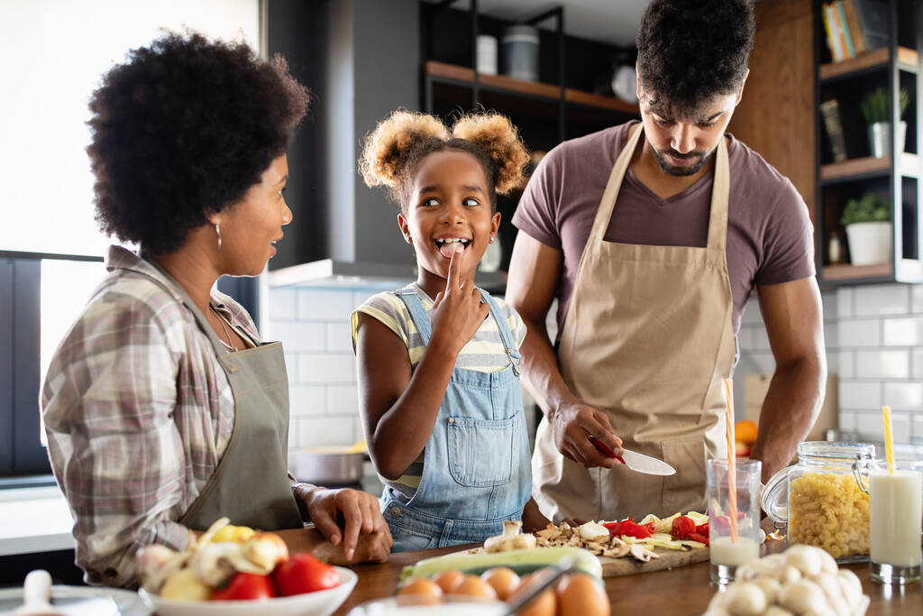 Здоровое питание дома. Счастливая чернокожая семья на кухне, веселясь и готовя вместе - Фото, изображение