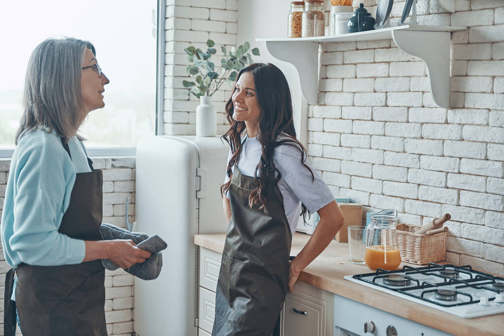 Schöne junge Frau und ihre Mutter kommunizieren während sie Zeit in der häuslichen Küche verbringen - Foto, Bild