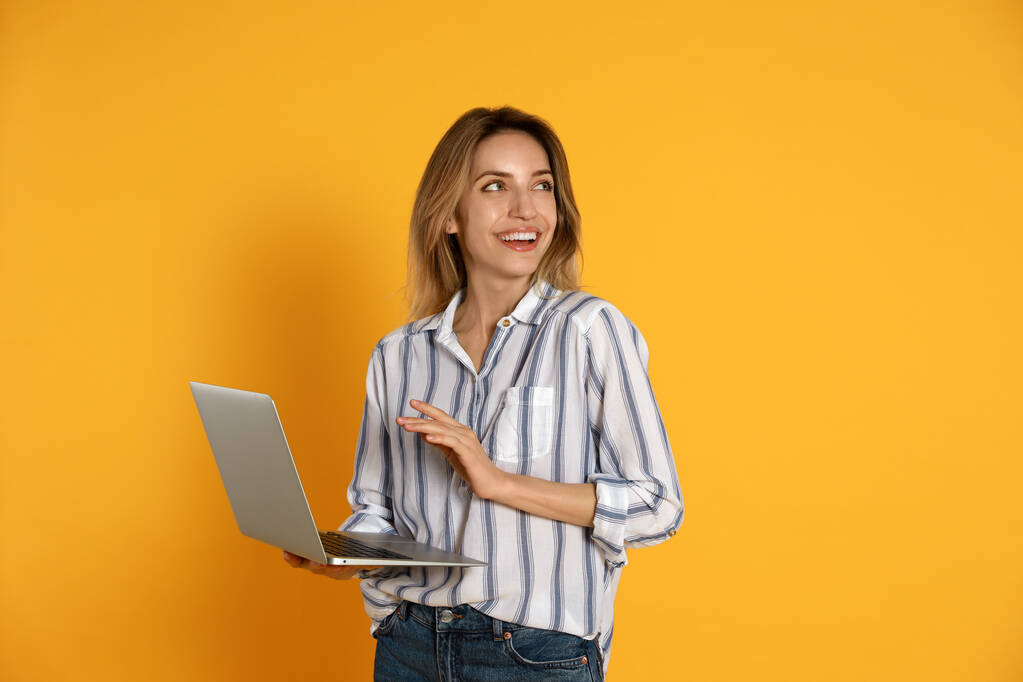 Giovane donna con computer portatile moderno su sfondo giallo - Foto, immagini