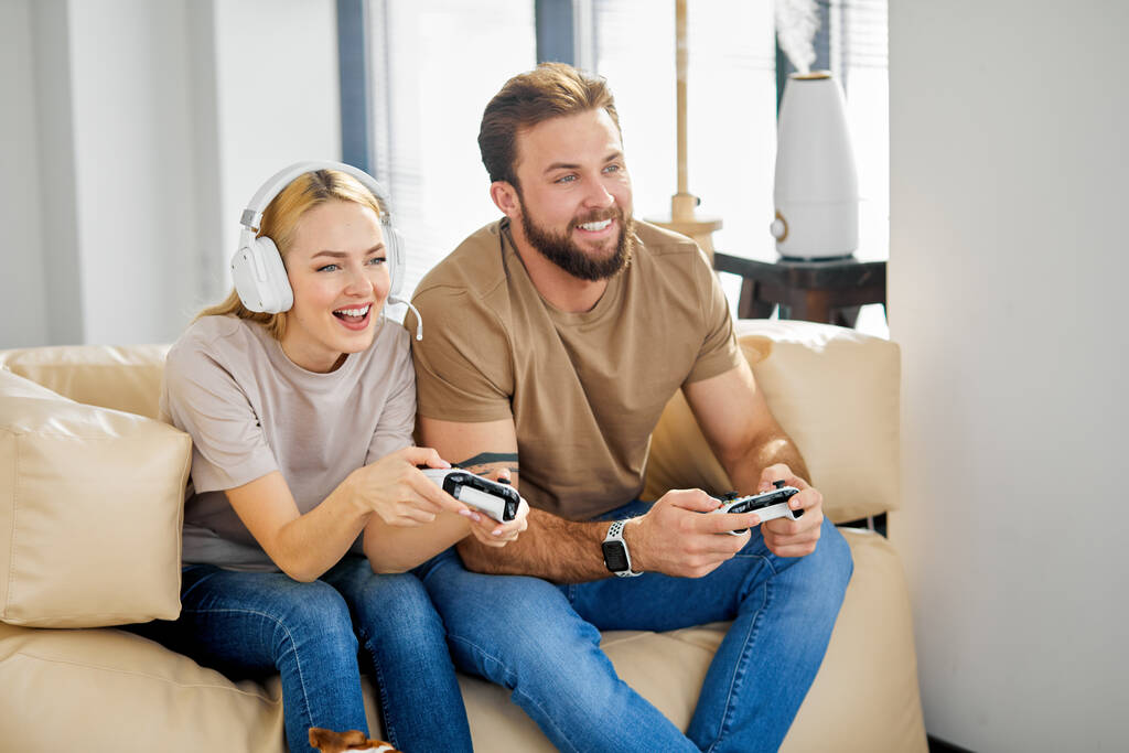 Cheerful man and woman sitting on sofa in living room playing computer video game - Fotó, kép