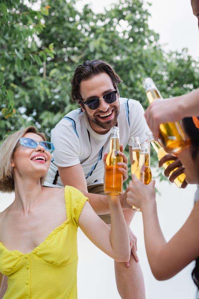 счастливые друзья в солнечных очках, звенящие бутылки пива во время летней вечеринки - Фото, изображение