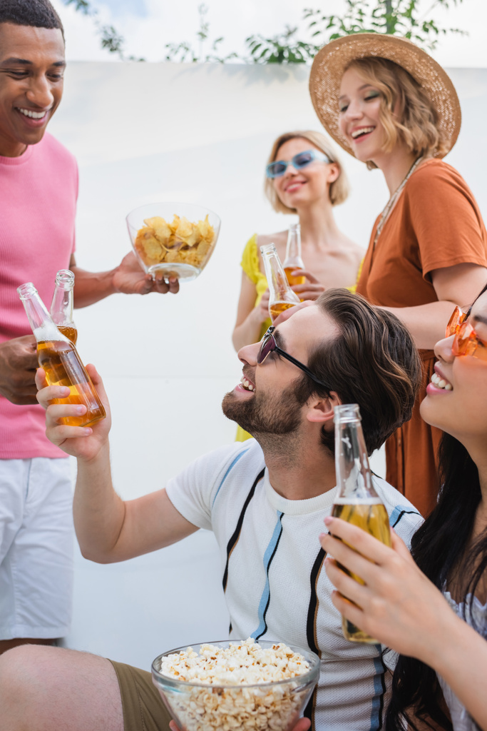 щасливі міжрасові чоловіки смердять пляшками пива біля усміхнених жінок
  - Фото, зображення