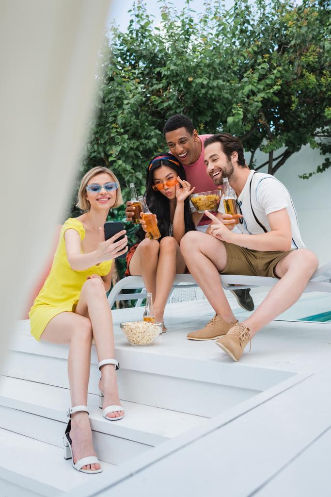 mujer feliz tomando selfie en el teléfono móvil durante la fiesta con amigos multiétnicos, borrosa primer plano - Foto, Imagen