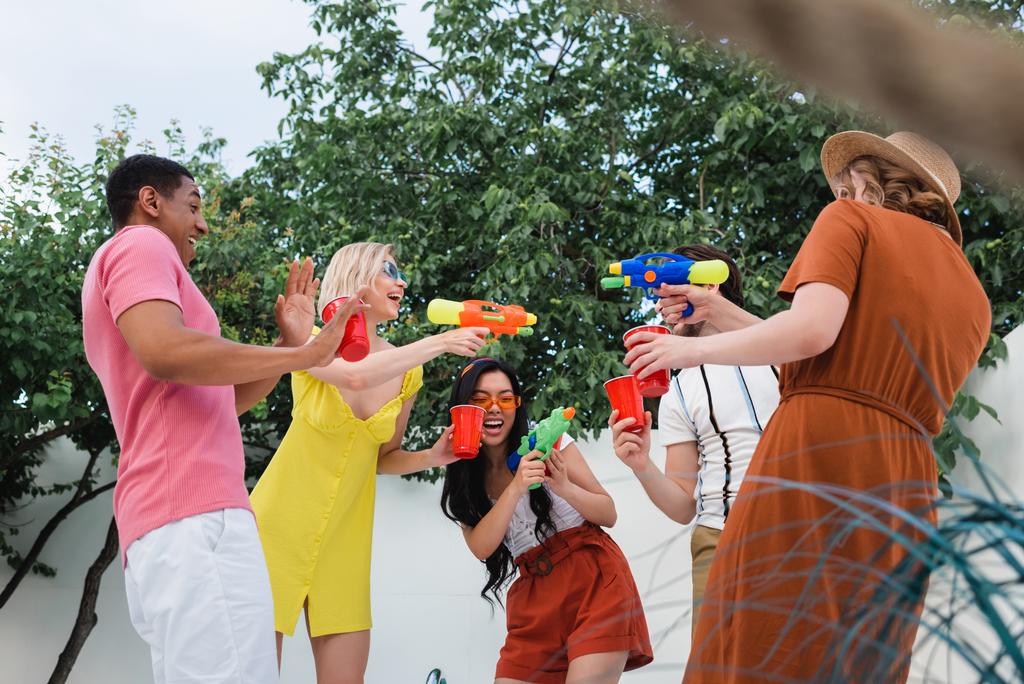 веселі жінки грають з водяними пістолетами біля сміху багатоетнічних друзів
 - Фото, зображення