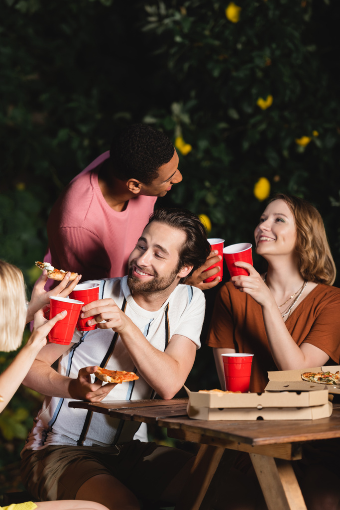 Багатоетнічні друзі з піцою та пластиковими чашками розмовляють під час вечірки
  - Фото, зображення
