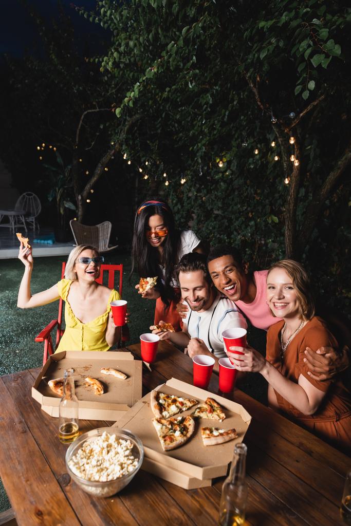 夏のパーティーで楽しいビール、ピザ、ポップコーンを持つ幸せな多民族の友人  - 写真・画像
