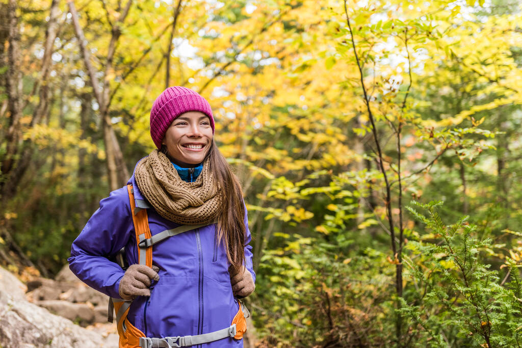 Happy asian woman hiking in autumn forest nature walking on trail path. Hiker girl with backpack, hat, scarf and jacket on fall adventure travel outdoors good weather during hike in cold weather. - Foto, Imagen