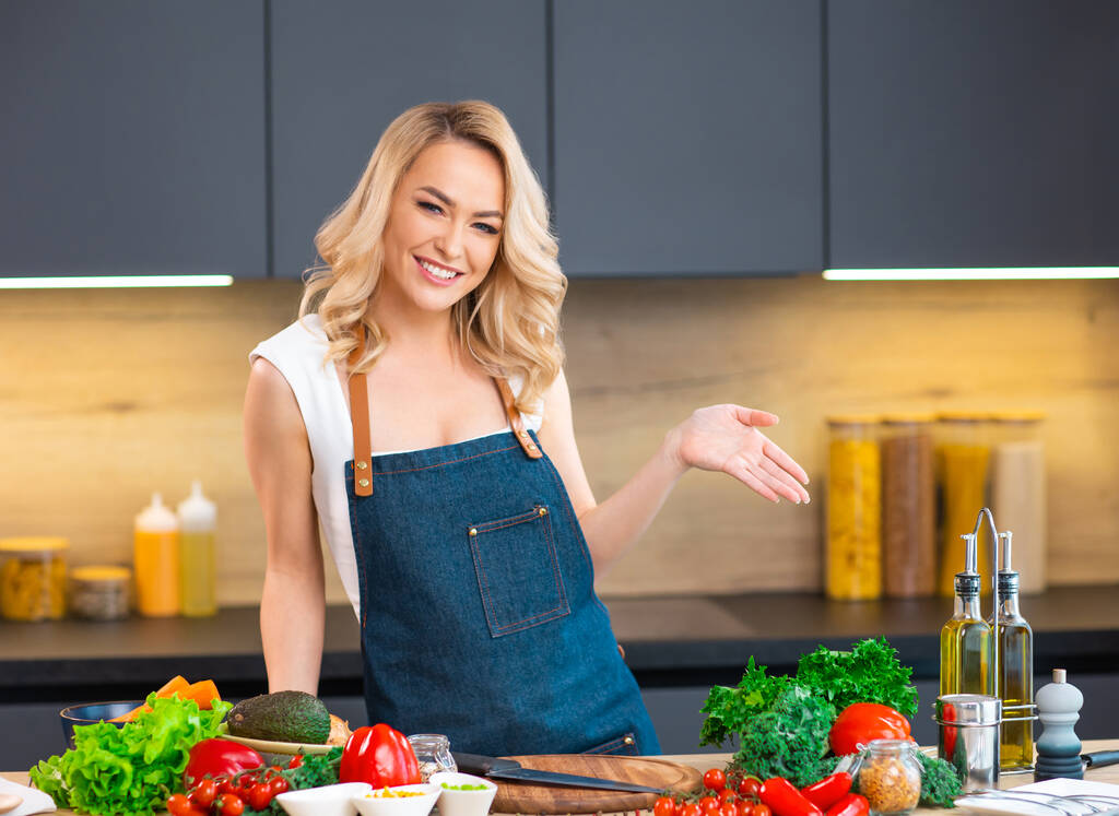 Young woman prepares food and hosts a cooking show. The blogger streams from modern kitchen. Vegetarian healthy food preparation. - Photo, Image