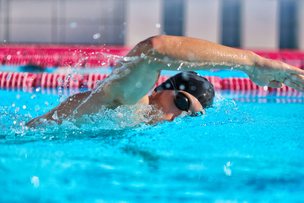 Swimmer man doing crawl swim in swimming pool portrait. Closeup of athlete wearing goggles, swimming cap training in blue water indoors - Foto, imagen