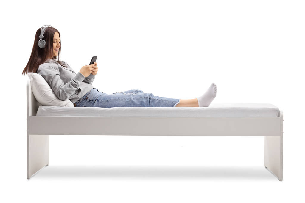 Женщина-подросток с наушниками, лежащих в кровати изолированы на белом фоне - Фото, изображение