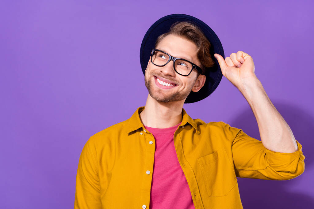 Photo of young handsome man happy positive smile hand touch hat dream look empty space isolated over violet color background - 写真・画像