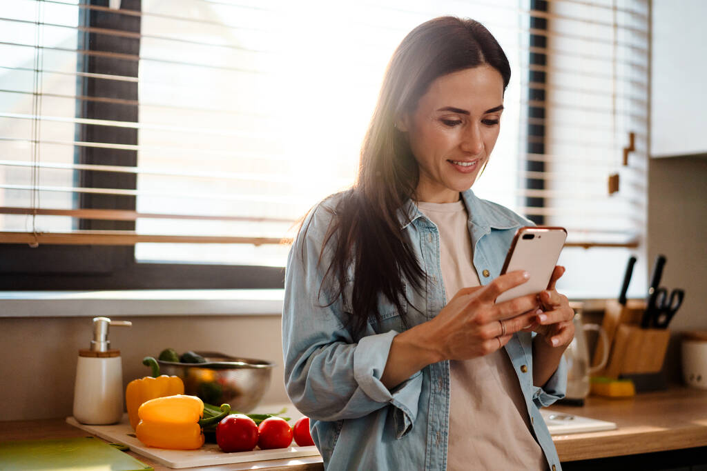 Lächelnd attraktive junge Frau SMS auf Handy in der Küche - Foto, Bild