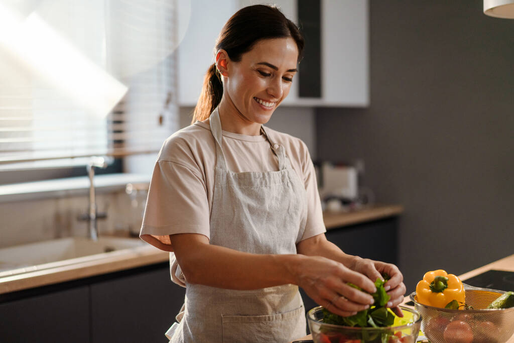 家庭のキッチンで野菜とサラダを作る魅力的な女性の笑顔 - 写真・画像
