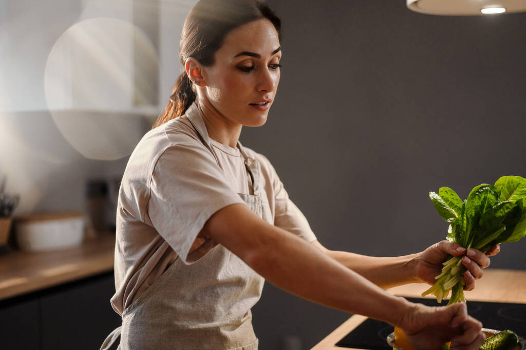 Összpontosított bájos nő, hogy salátát zöldségekkel otthon konyha - Fotó, kép