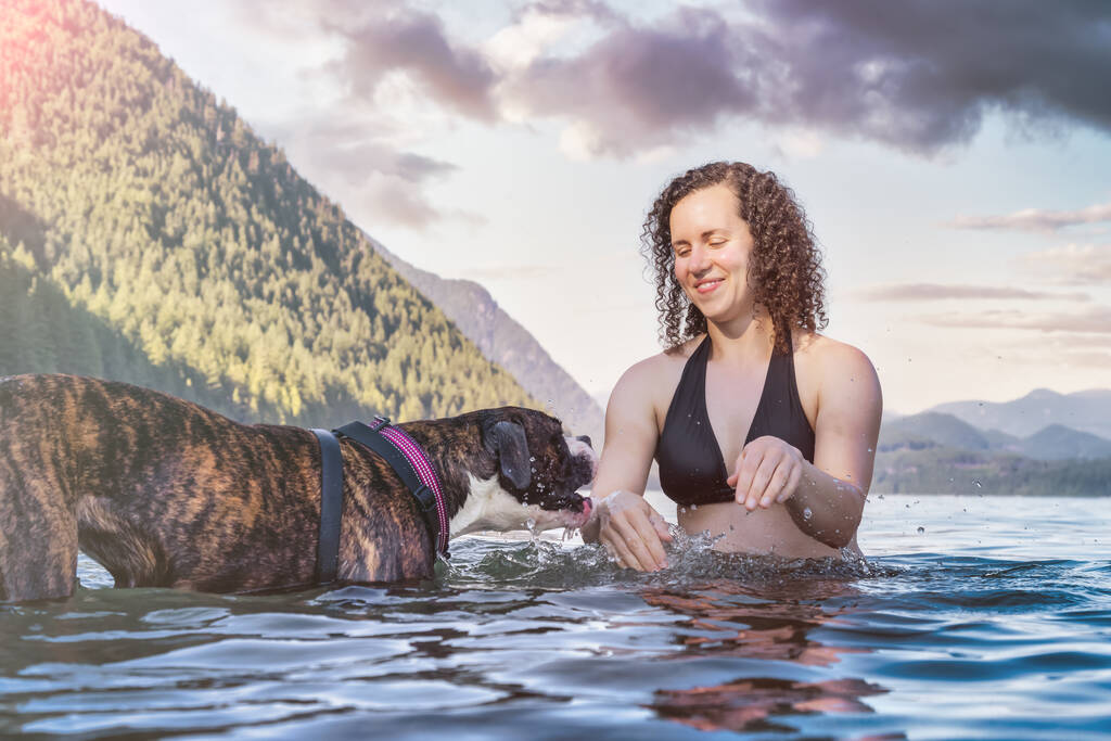 Кавказька жінка плаває в озері з собакою. - Фото, зображення