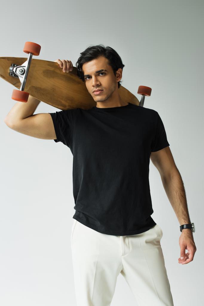 junger Mann in schwarzem T-Shirt hält Longboard isoliert auf grau - Foto, Bild