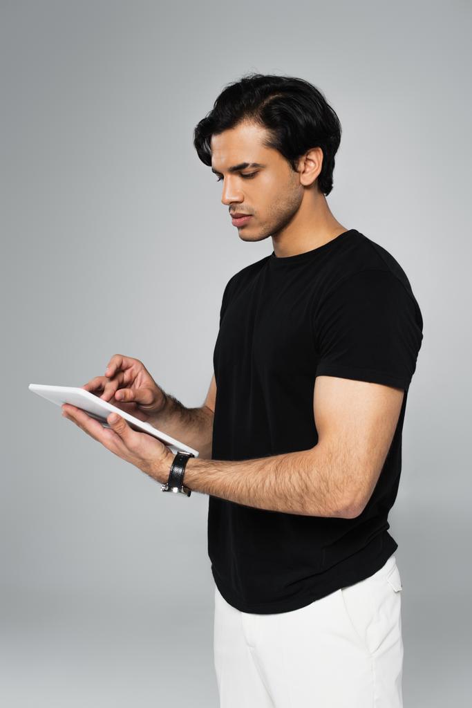 νεαρός άνδρας με μαύρο t-shirt χρησιμοποιώντας ψηφιακό δισκίο απομονωμένο σε γκρι - Φωτογραφία, εικόνα