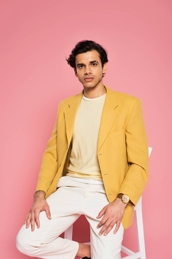jonge man in gele blazer zitten op witte stoel geïsoleerd op roze - Foto, afbeelding