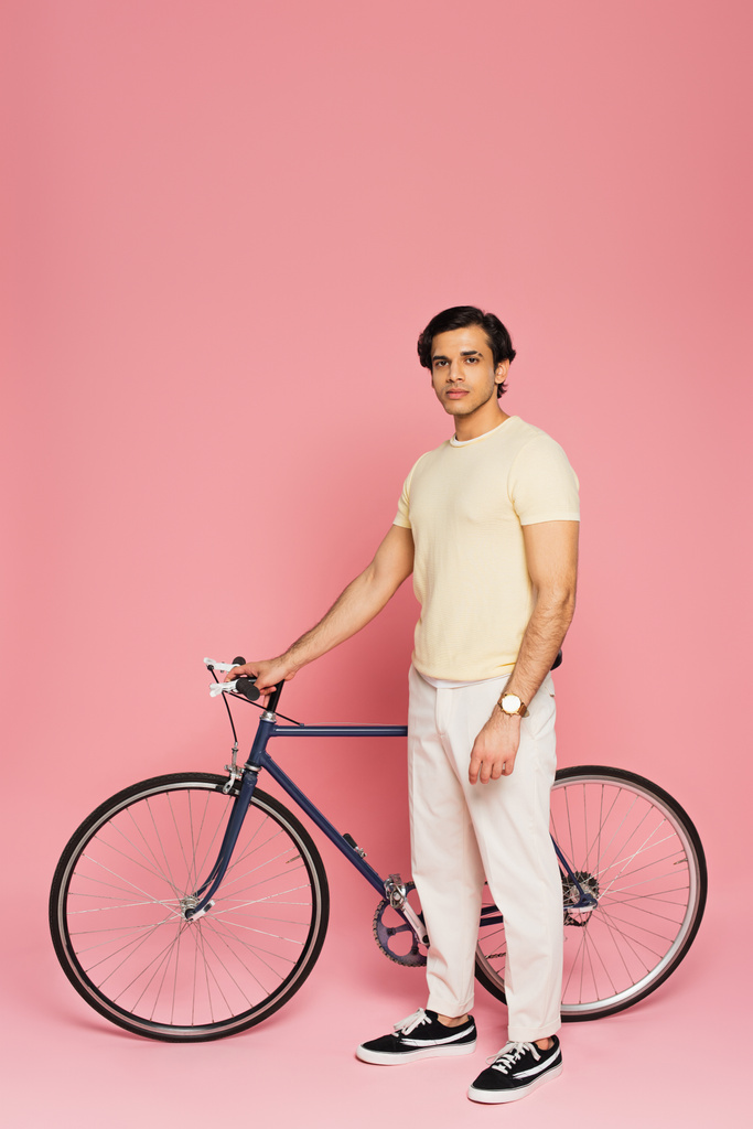 πλήρες μήκος του νεαρού άνδρα στέκεται κοντά ποδήλατο σε ροζ - Φωτογραφία, εικόνα