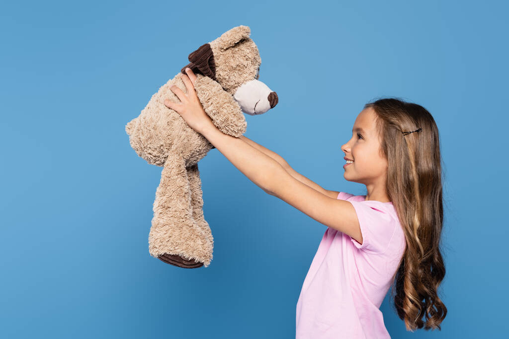Side view of girl holding soft toy isolated on blue  - Photo, Image