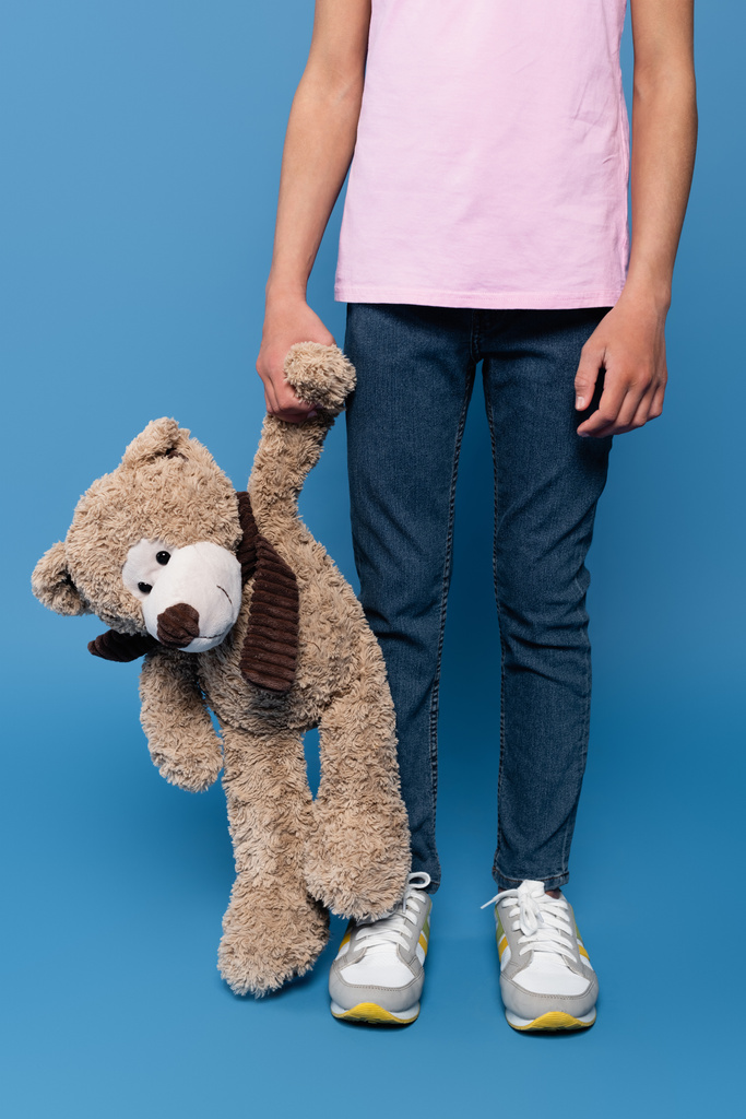 Καλλιεργημένη άποψη του παιδιού που κρατά αρκουδάκι σε μπλε φόντο  - Φωτογραφία, εικόνα