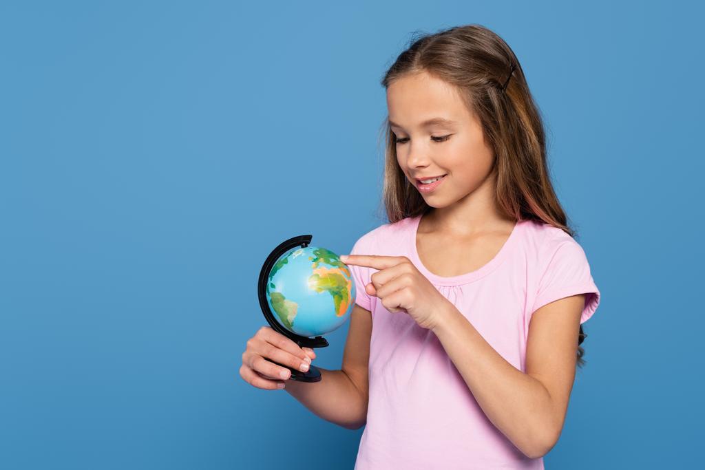 Cheerful child pointing at globe isolated on blue - Foto, Imagen
