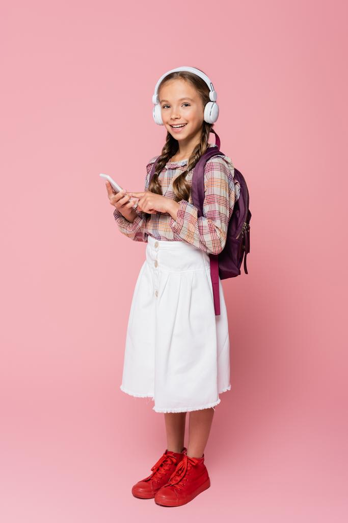 Preteen školák ve sluchátkách držící smartphone na růžovém pozadí  - Fotografie, Obrázek