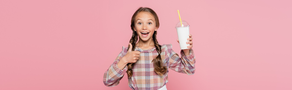 Wesoły dzieciak pokazując jak gest i trzymając milkshake odizolowany na różowym, sztandar  - Zdjęcie, obraz