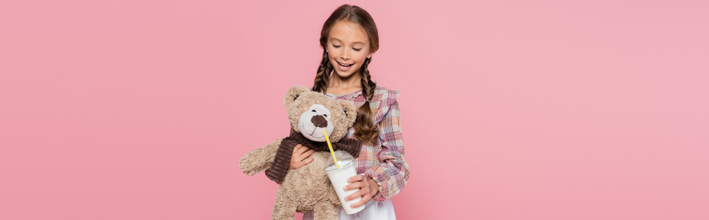 Preteen girl holding milkshake near teddy bear isolated on pink, banner  - Foto, imagen
