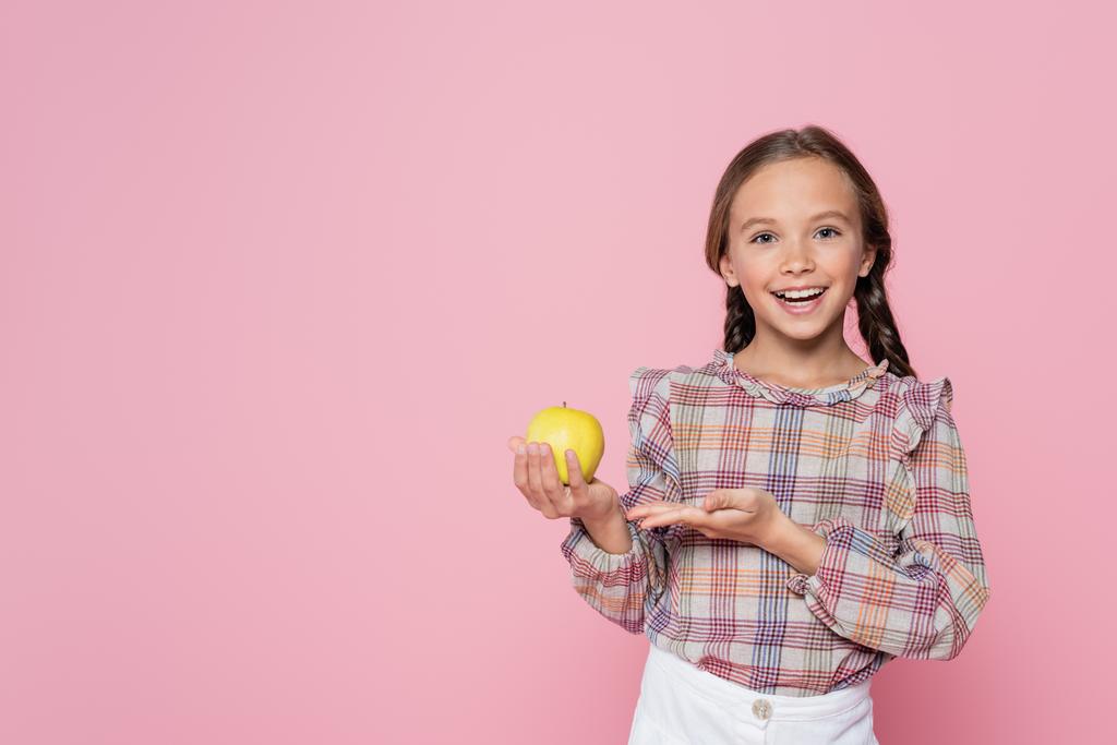 fröhliches Kind in karierter Bluse, das auf grünen Apfel auf rosa zeigt - Foto, Bild