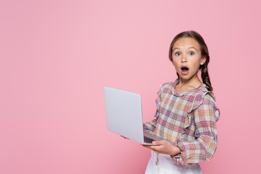 erstaunt Mädchen mit Laptop Blick auf Kamera isoliert auf rosa - Foto, Bild