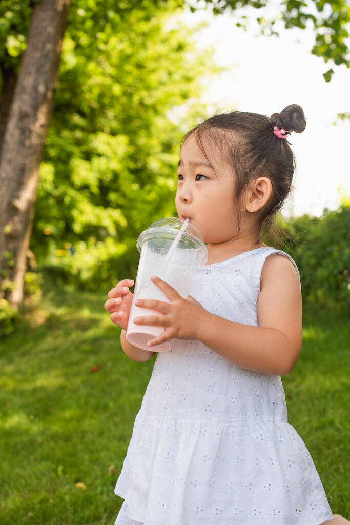 Asyalı küçük kız giyinmiş Parkta lezzetli milkshake içiyor - Fotoğraf, Görsel